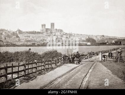 A late 19th century view of farm workers in the fields near Lincoln, a cathedral city and county town of Lincolnshire in the East Midlands of England.  Called Lindum Colonia in Roman times it developed from an Iron Age settlement on the River Witham. The English Gothic Lincoln Cathedral, once the world's tallest building for over 200 years can be seen towering over the town. Stock Photo