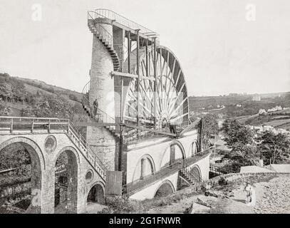 A late 19th century view of Laxey Wheel (also known as Lady Isabella) is built into the hillside above the village of Laxey in the Isle of Man. The largest working waterwheel in the world with a 72-foot-6-inch (22.1 m) diameter, revolving at approximately three revolutions per minute. It was designed by Robert Casement in 1854 to pump water from the Great Laxey Mines industrial complex, employing over 600 miners at its peak, producing lead, copper, silver and zinc, until it closed in 1929. Stock Photo