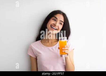 Summer detox and healthy eating concept. Smiling Indian woman with glass of fresh orange juice against white wall Stock Photo