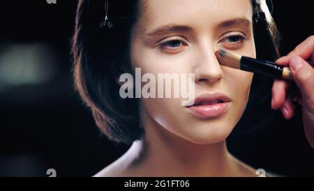 makeup artist applying makeup foundation on skin of model with cosmetic brush Stock Photo
