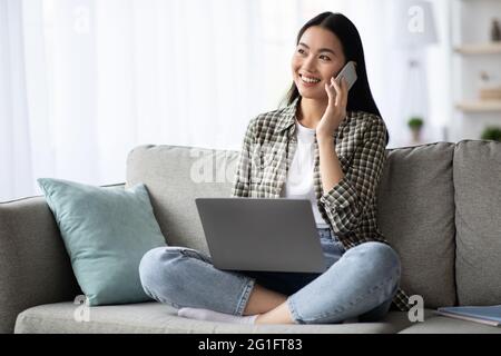 Pretty young woman having phone conversation, using laptop Stock Photo
