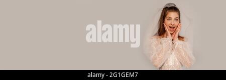 astonished woman in wedding dress touching face isolated on grey, banner Stock Photo