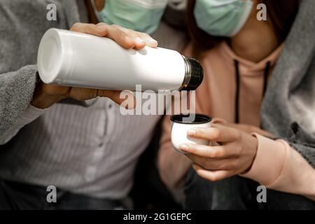 cropped view of tourists in medical masks pouring coffee from thermos Stock Photo