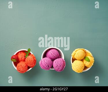 Gourmet flavours of Italian ice cream in vibrant colors served in individual paper cups on blue background. Strawberry sorbet, blueberry or lavender i Stock Photo