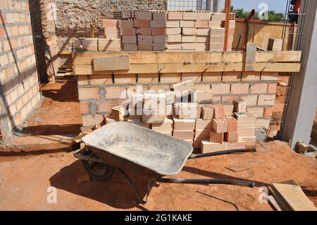 Wheelbarrow or trolley. Wheelbarrow used in construction site to load bricks, cement sand and various other products at the bottom of the block wall u Stock Photo