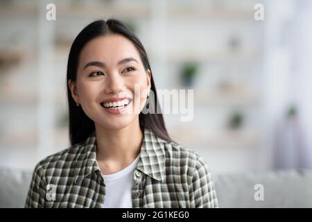 Joyful young asian lady sitting on couch at home Stock Photo