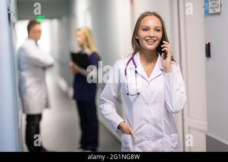 medicine, profession and healthcare concept. Happy smiling asian female doctor or nurse in blue uniform with stethoscope calling on smartphone over ho Stock Photo