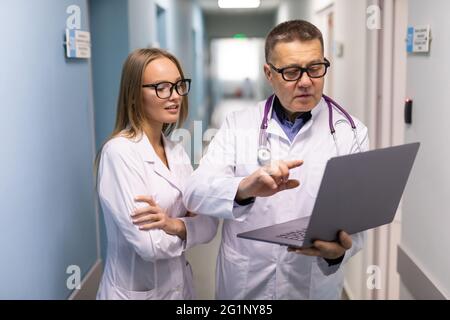 Photo of two doctors together discussing new way of treatment while having a meeting. Doctors using laptop while discussing new way of treatment. Stock Photo