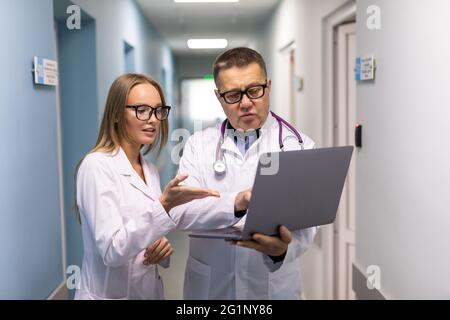 Photo of two doctors together discussing new way of treatment while having a meeting. Doctors using laptop while discussing new way of treatment. Stock Photo