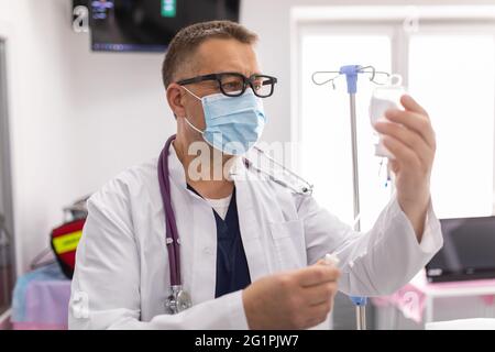 Doctor take care or look after patient by himself. Doctor checking Intravenous drip, I.V. tube saline fluid bag for cure patient in hospital room. He Stock Photo