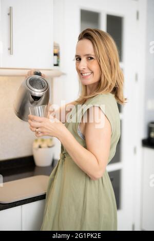 Young woman pouring water into glass in kitchen Stock Photo