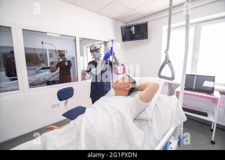 Doctor making injection using dropper. Covid 19 treatment. Female doctor in protective clothes give treatment via dropper for mature patient in hospit Stock Photo