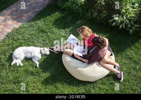 teenagers 16-17 years old, a guy and a girl, are sitting in large soft pouf on grass, reading books. distance learning, preparation for exams. Young p Stock Photo