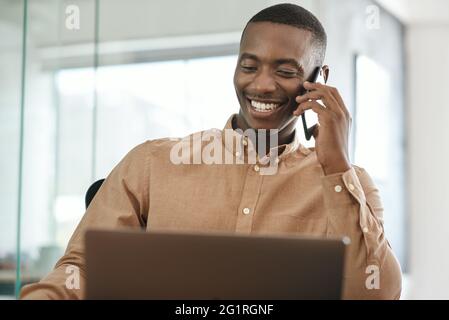 Young African businessman talking on his cellphone while using a laptop Stock Photo