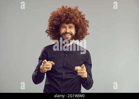 Toothy smiling confident business man in funny afro hair wig pointing at camera Stock Photo