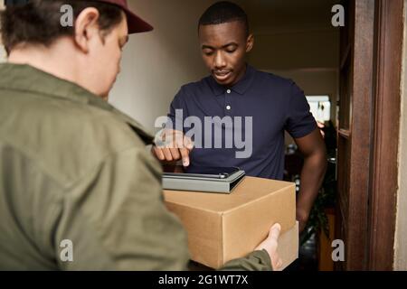 Young African man digitally signing for a courier delivery Stock Photo