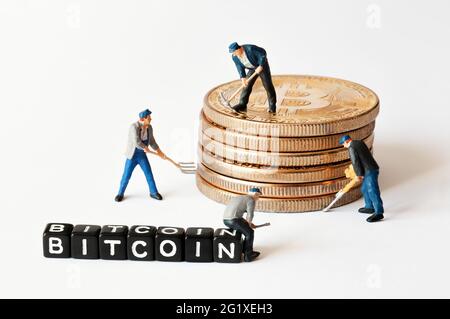 Group of miner figurines with equipment working on stack of bitcoins near black cubes with Bitcoin text. Cryptocurrency, blockchain or trading concept Stock Photo