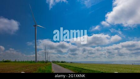 Under the blue sky with white clouds, the propeller of the green electricity generator is mounted on the side of the road in the field Stock Photo