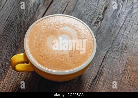 Yellow cup of cappuccino with latte art on wooden table Stock Photo