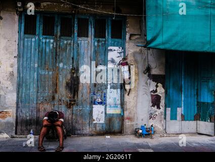 A tired looking man sleeps while sitting in front of an old building in Chinatown, Bangkok, Thailand Stock Photo