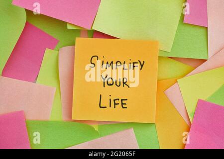 A yellow paper note with the phrase Simplify Your Life written on it with some colorful paper notes below it. Close up. Stock Photo