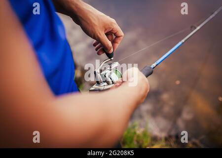 Young man fishing on river. Closeup of fisherman holding rod. Professional fishing equipment. Spinning Stock Photo