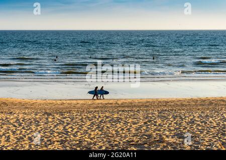 Surfers in the ocean and surfers walking on the beach in Faro, Algarve, Portugal Stock Photo