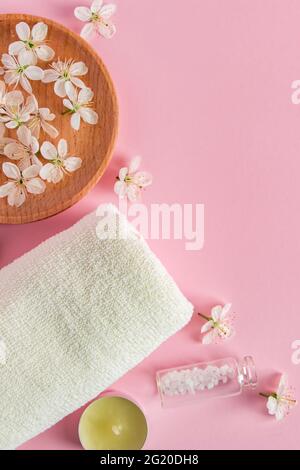 Cosmetic products for spa and aromatherapy. Candles, sea salt, towel and flowers on a pink background. Skin care and beauty concept. Place for your te Stock Photo