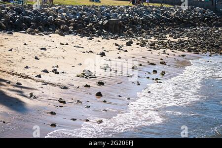 gentle waves peacefully lapping the edge of a section of riprap reinforced beach on Coronado Island near San Diego in California with shimmering sunli Stock Photo