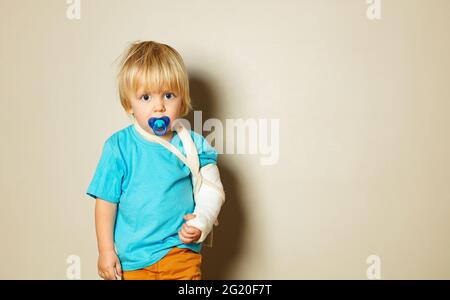 Sad boy with pacifier and broken hand in plaster Stock Photo