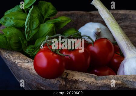 close up of tomatoes, basil leaves and garlic in a old wooden bowl Stock Photo