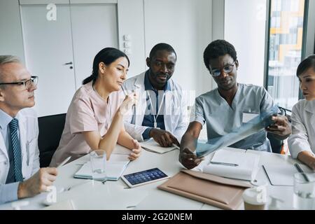 Diverse group of medical professionals working together at meeting table during council or conference Stock Photo