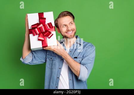 Photo portrait of young guy smiling in denim shirt trying to guess what in present curious isolated on vivid green color background Stock Photo