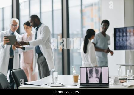 Diverse group of doctors collaborating in conference room with focus on laptop screen in foreground, copy space Stock Photo