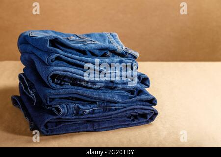 Stack of blue denim clothes. Pile folded blue denim pants in different shades of blue on brown craft background with copy space Stock Photo