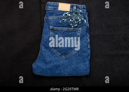 Flower in jeans pocket. Beautiful blue white flower in pocket of blue jean pants on black denim background. Spring outfit Stock Photo