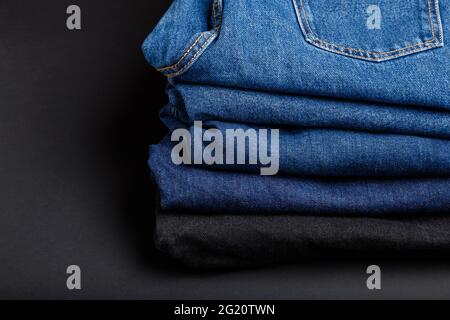 Blue jeans trousers stack. Stack of blue jeans on black background with copy space. Stock Photo