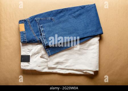 White Blue jeans pants. Assortment of different color denim clothing in store shop with emty label. White denim jean pants, blue jeans on brown table. Stock Photo