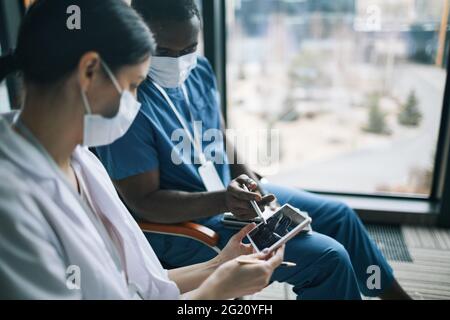 Side view portrait of two doctors wearing masks while looking at digital tablet Stock Photo