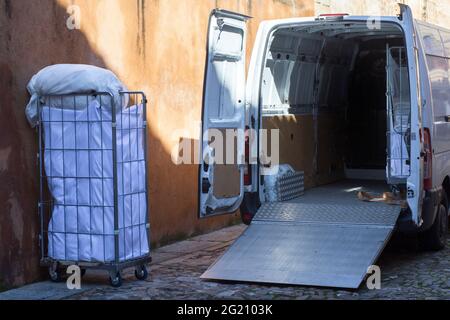 Picking dirt laundry carts. The van equipped with lift ramp is parked in an old town city Stock Photo