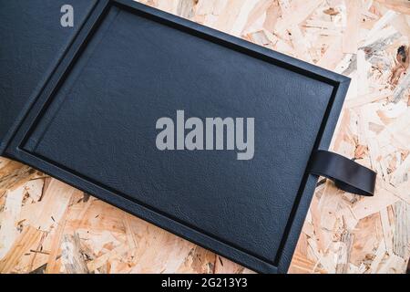 Black leather photo album on a table with vintage wood background. Wedding or family photo book memories with a nice leather box. Family value memory. Stock Photo