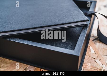 Black leather photo album on a table with vintage wood background. Wedding or family photo book memories. Family value memory. Stock Photo