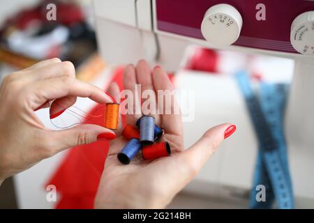 Close-up of female seamstress holding on palm colourful reels of thread Stock Photo