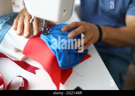 Close-up of professional atelier worker using sewing machine. Man in protective uniform Stock Photo