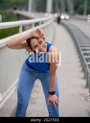 Athlete resting wiping sweat from forehead on bridge. Attractive girl running jogging exercising outdoors. Stock Photo