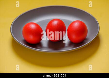 Colorful traditional painted Easter eggs. Red eggs, yellow background. Three eggs in a gray plate on a yellow background. Colors 2021 Stock Photo
