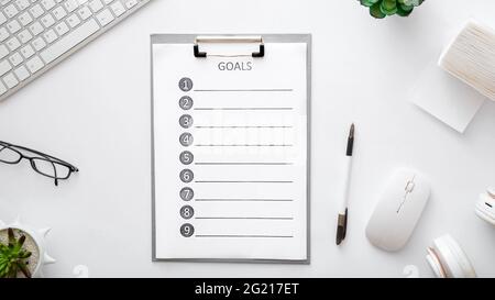 Goals list on workspace on white background. Flat lay, top view office table desk. New ideas on home work space with keyboard mouse glasses papers Stock Photo