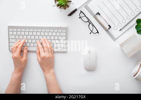Female hands typing on keyboard at white table workplace. Home office workspace with keyboard mouse glasses. Flat lay woman hands on white desk use pc Stock Photo