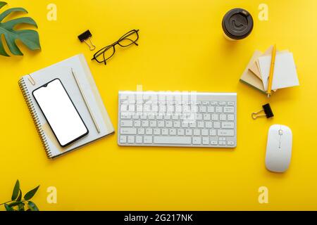 Flat office workspace on colorful yellow background. Office table desk with computer keyboard, glasses, smartphone mouse, office supplies plants Stock Photo