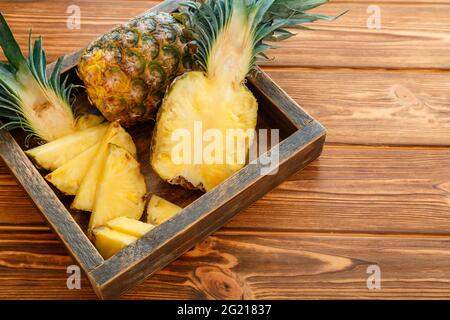 Sliced Pineapple. Bromelain tropical summer fruit pineapple halves and whole pineapple on brown dark table in wooden box with copy space Stock Photo
